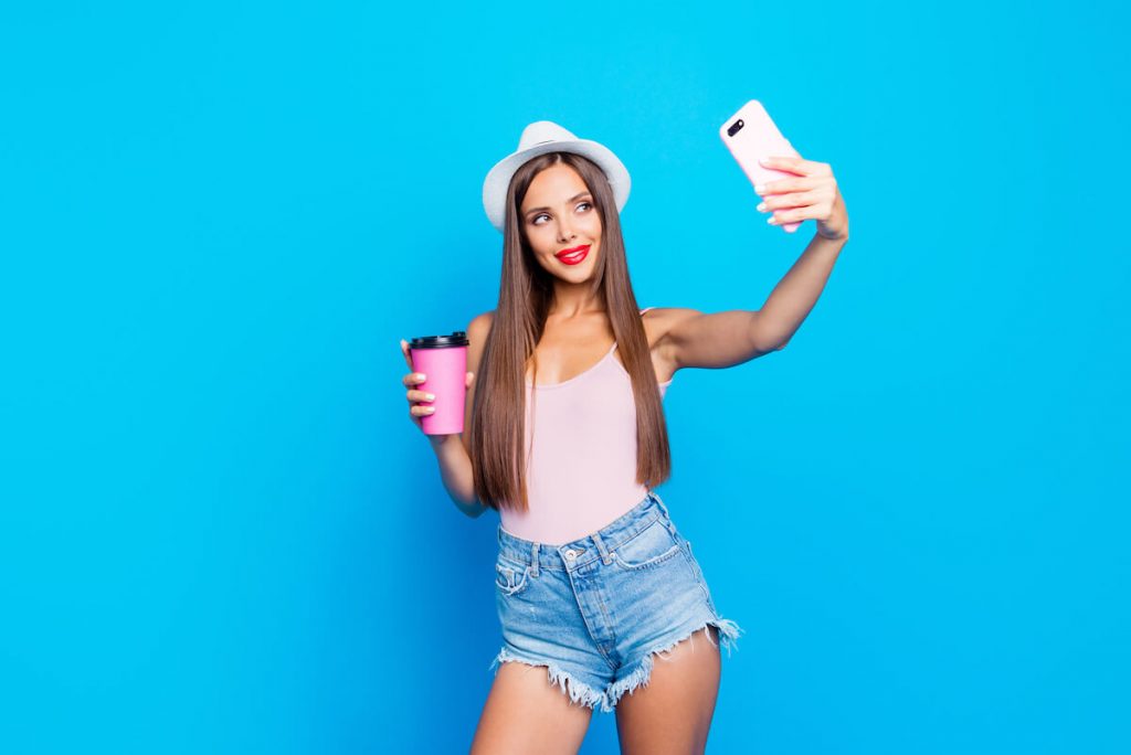 Influencer taking a selfie in front of a blue wall: how to reach out to brands as an influencer